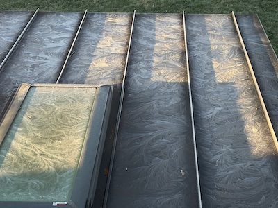 A floral frost pattern on a black metal roof and skylight window, one April morning in New England